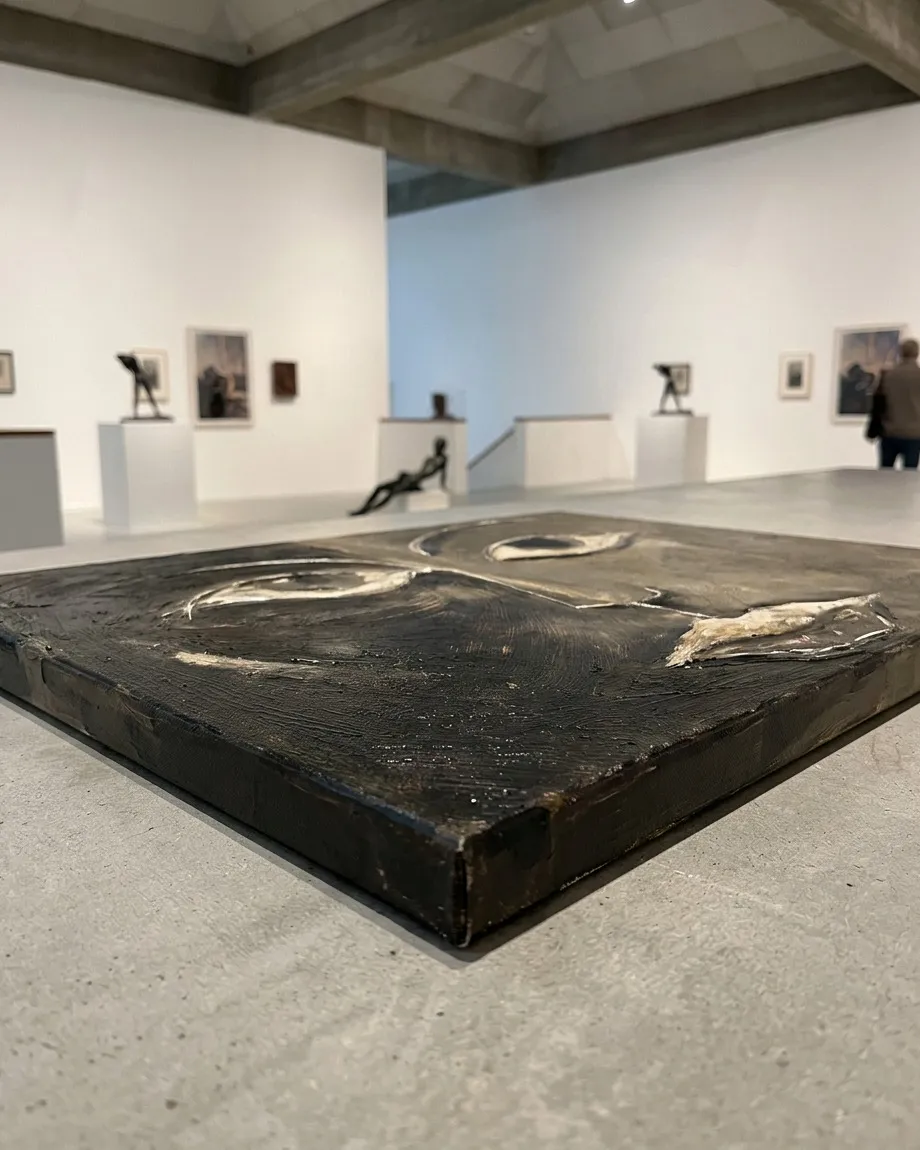 Perspectiva rasante del lienzo acostado sobre una losa gris en una sala de museo, destacando el relieve de las incisiones de los ojos y la boca.