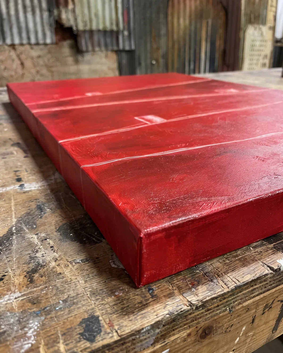 Plano de detalle lateral de la obra de arte abstracto ATHAR en rojo carmesí con textura de óleo y finas incisiones blancas sobre una mesa rústica de madera de taller.
