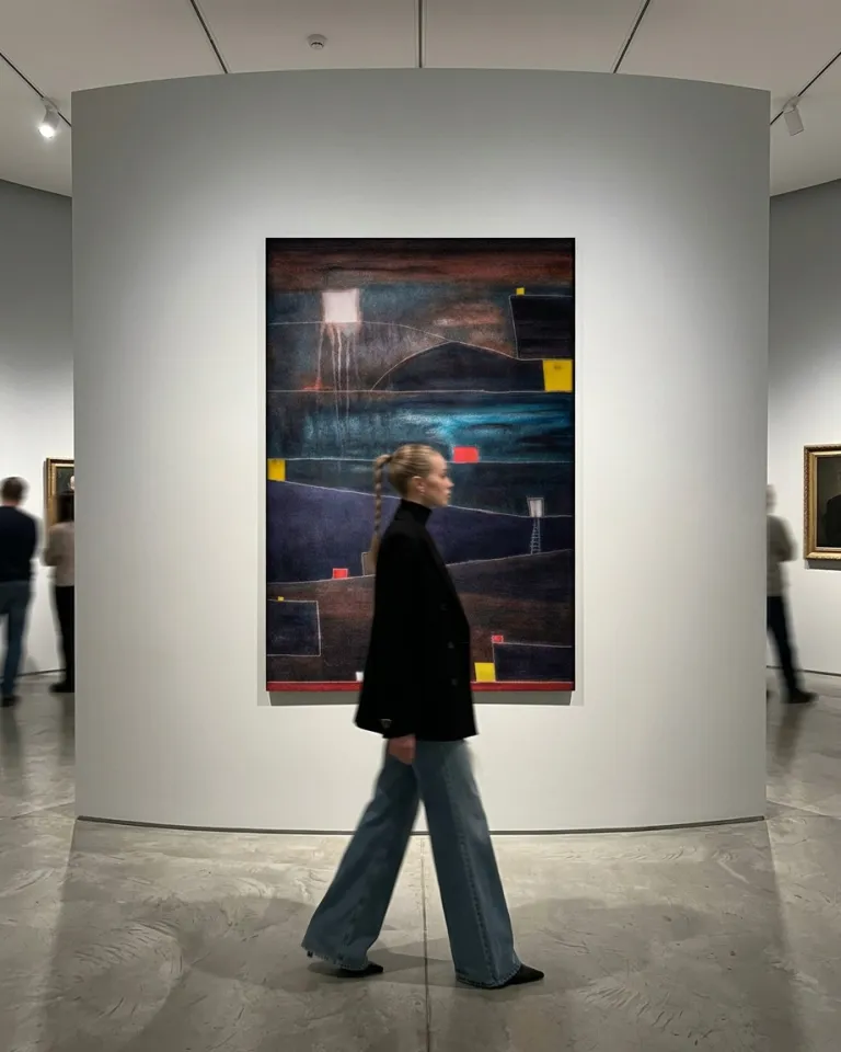 ADITUS by Maurizio Valch, an 80 by 120 cm vertical abstract painting installed on a curved gallery wall, with a visitor walking in front of it. The work combines dark bands, turquoise, and red and yellow accents.