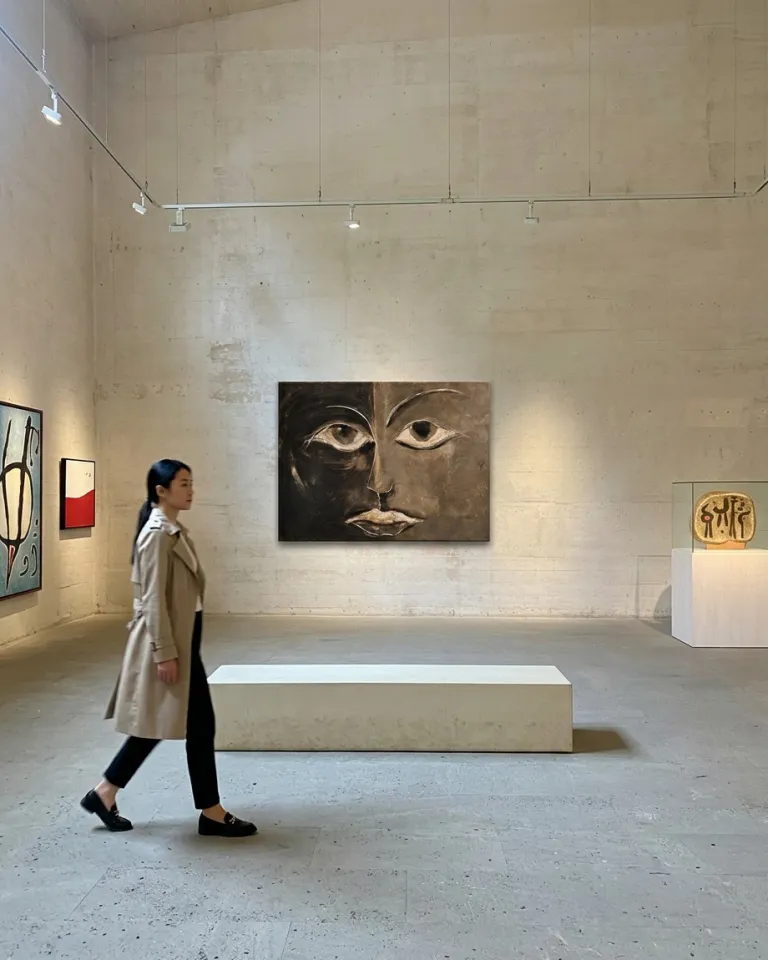 Installation of the artwork 'La mitad de la mirada' hanging on a rustic textured gallery wall, with a person walking in the foreground in front of it.