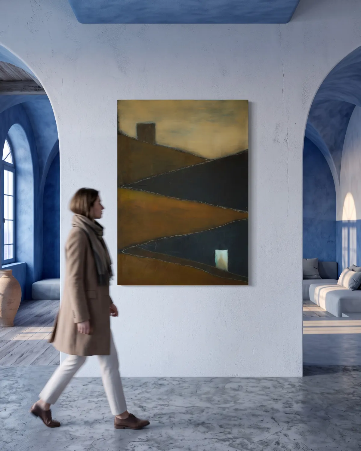 A vertical abstract painting hangs on a white plaster wall flanked by blue, Greek-style arched doorways. The painting features diagonal sections of ochre and dark blue, with a dark block at the top and a small white rectangle in the lower right. In the foreground, a woman in a beige coat walks past, captured with a subtle motion blur effect.