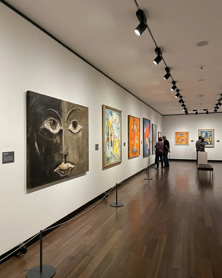 Perspective view of the artwork by Maurizio Valch hanging on the white wall of a museum hallway, illuminated by spotlights, with a wooden floor.