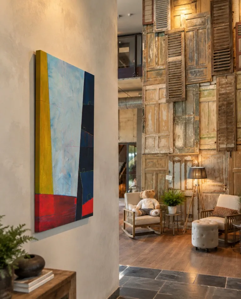 LIMEN by Maurizio Valch hangs on a light wall in a warm interior, beside a group of old wooden doors and shutters.
