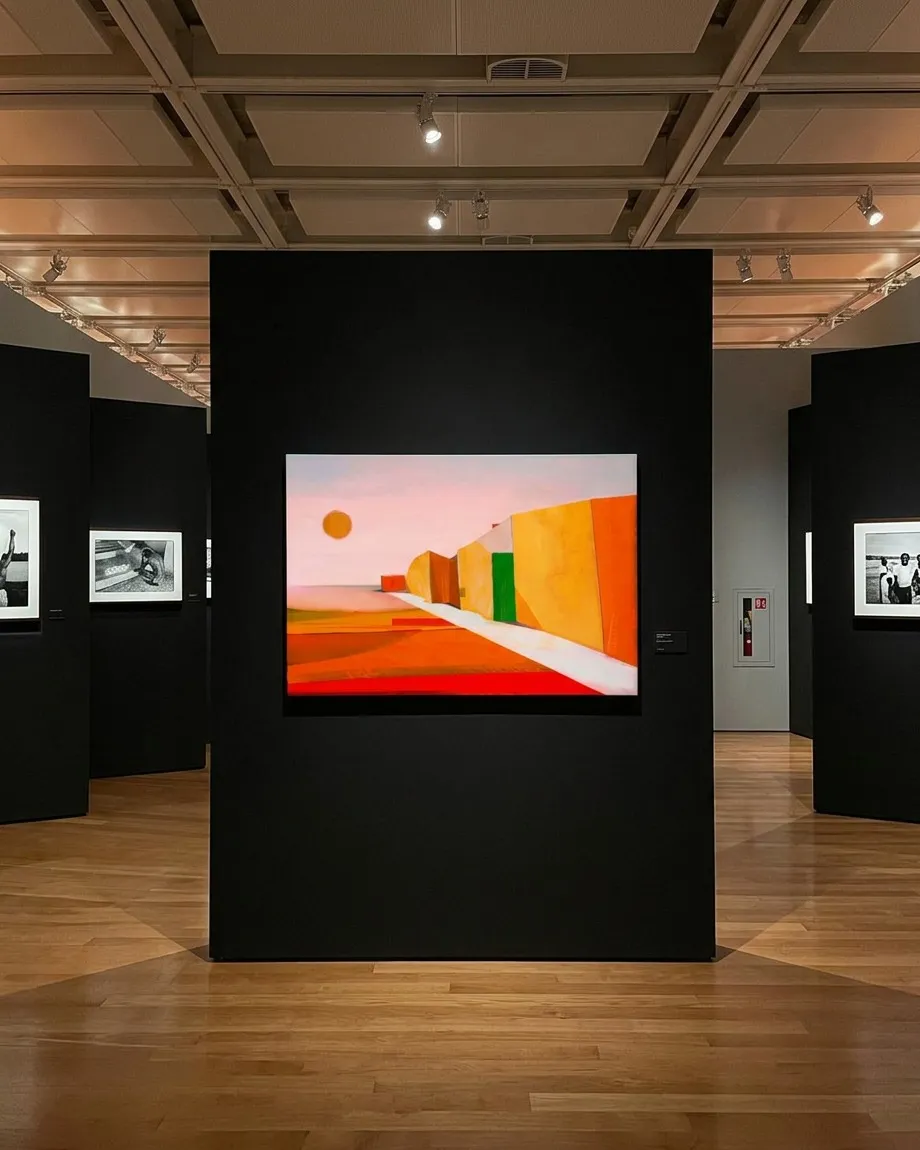 VIA SOLIS by Maurizio Valch displayed on a black museum panel; the painting shows a white path between red, yellow, and green planes beneath an orange sun.