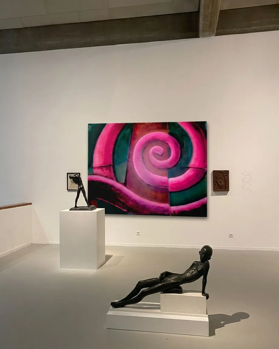 El cuadro VORAGO colgado en una sala blanca de museo, flanqueado por esculturas figurativas de bronce sobre pedestales.