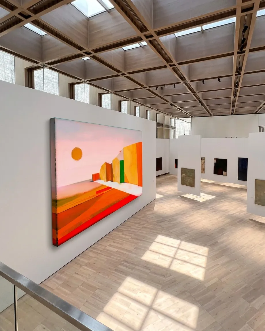 VIA SOLIS, a painting by Maurizio Valch, installed in a large museum gallery with a gridded ceiling and overhead light; it shows a white path between red, orange, and yellow fields, vertical blocks, and an orange sun against a pink sky.