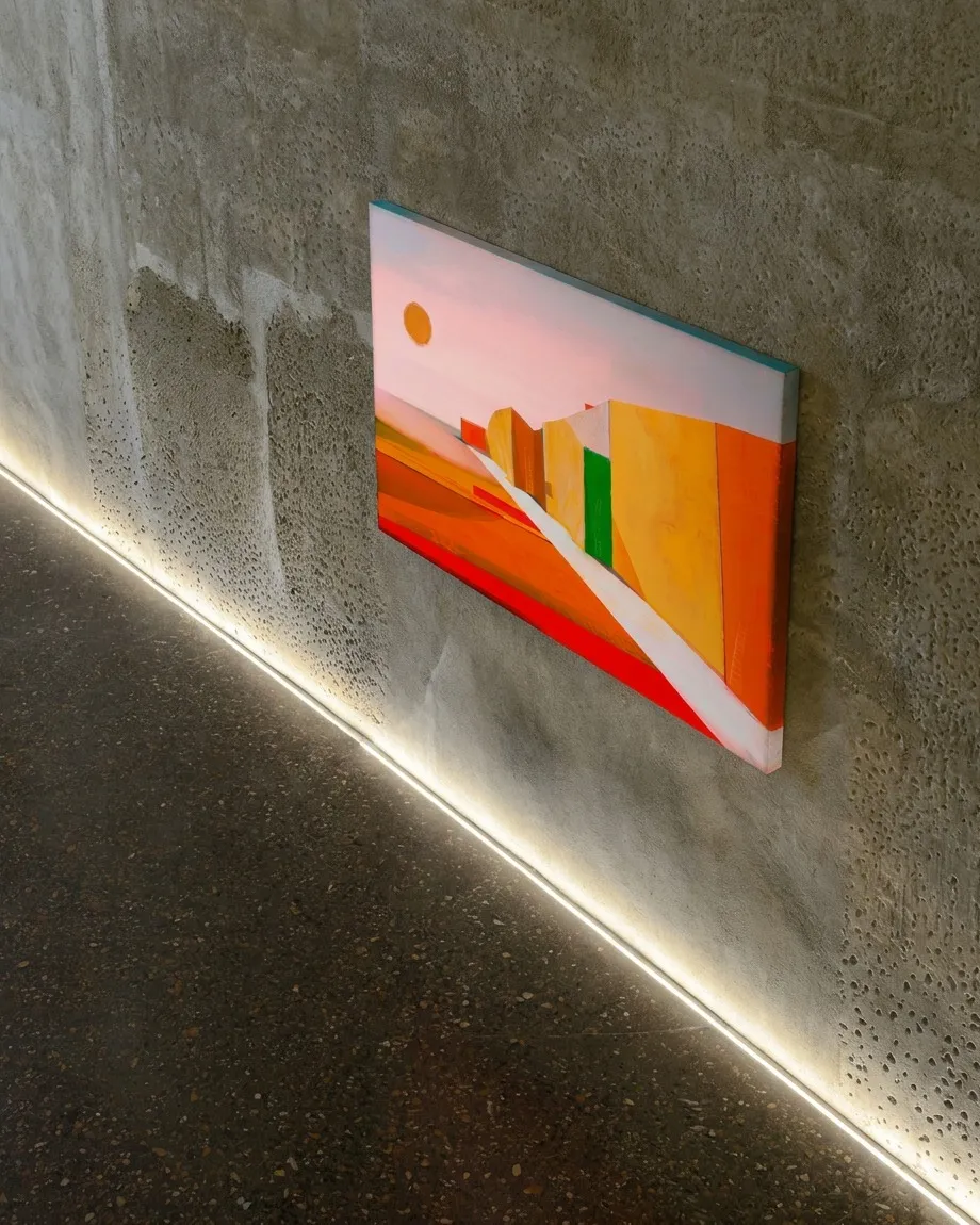 VIA SOLIS de Maurizio Valch, pintura abstracta de tonos rojos, naranjas y amarillos con una vía blanca, instalada en un muro de hormigón texturado.