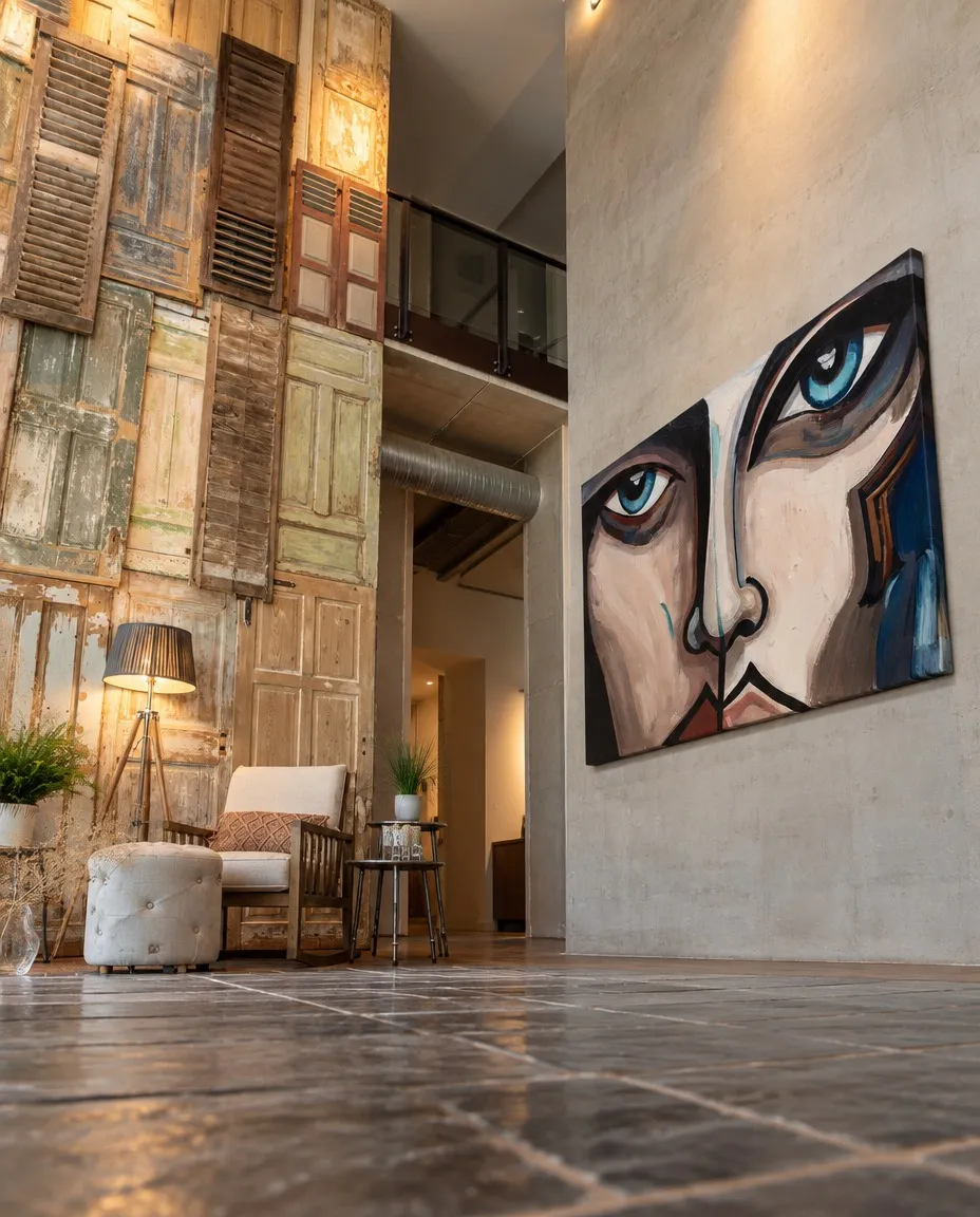 CUTIS de Maurizio Valch, gran pintura de rostro fragmentado con ojos azules, presentada en la pared de un loft industrial con contraventanas antiguas.