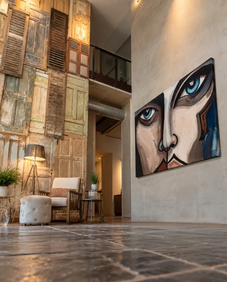 CUTIS de Maurizio Valch, gran pintura de rostro fragmentado con ojos azules, presentada en la pared de un loft industrial con contraventanas antiguas.