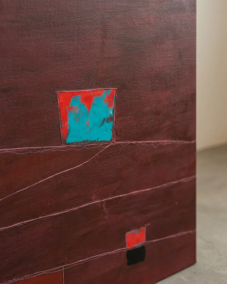 Vista cercana de una pintura abstracta. Predomina un campo carmesí oscuro. Un bloque rectangular de color azul turquesa vibrante con textura áspera se inserta en la parte superior central. Líneas finas incisas de color claro atraviesan horizontalmente la superficie. En la parte inferior derecha, un pequeño bloque rojo sobre una base negra. Se aprecia la textura del lienzo y las capas de pintura acrílica y óleo.