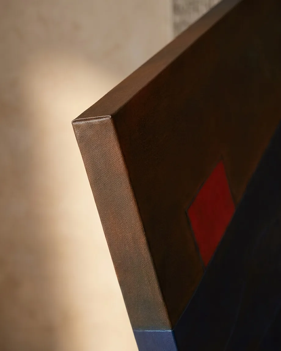 A close-up, oblique view of the top corner of a three-centimeter deep canvas. The woven texture of the fabric is visible along the dark brown painted edge. On the front surface, a vibrant red square sits adjacent to a deep indigo blue field under soft, indirect light against a neutral background.