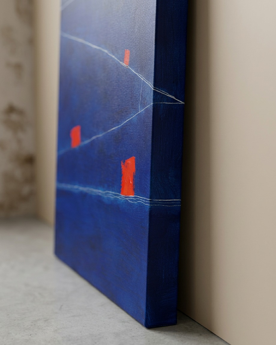 A close-up side view of an abstract painting, `Submerged Architectures`, with a deep blue background, vibrant red rectangular shapes, and thin white lines. The painting leans against a light beige wall, resting on a concrete floor.