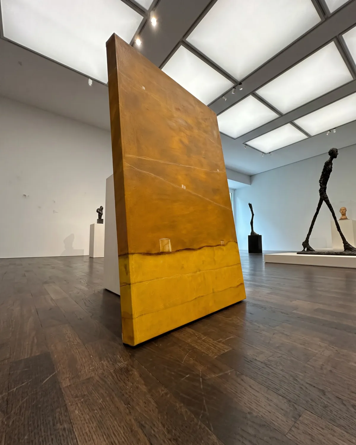 Vista en perspectiva de la obra QUINQUE en una sala de exposición junto a esculturas de estilo minimalista y brutalista.