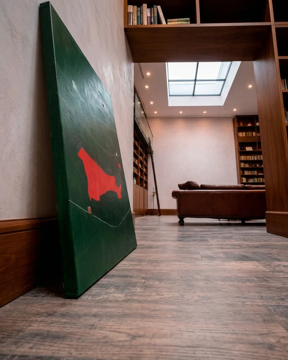 La pintura abstracta Sogno di un filo teso apoyada directamente en el suelo de madera de un estudio o biblioteca, bajo la luz natural de un tragaluz.